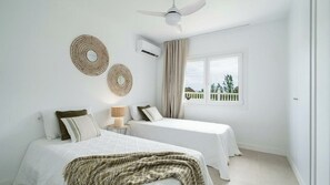 Ein Schlafzimmer mit zwei Betten, einem Deckenventilator, einer Klimaanlage und einem Fenster mit Blick.