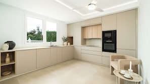 A modern kitchen with built-in appliances, a dining area with a table, and a window with a view of greenery. - Luxury Villa Mijas costa by Ruralidays (Málaga)