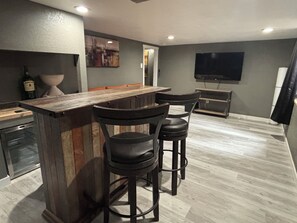 Uma área de bar com banquetas, balcão e uma televisão fixada na parede.