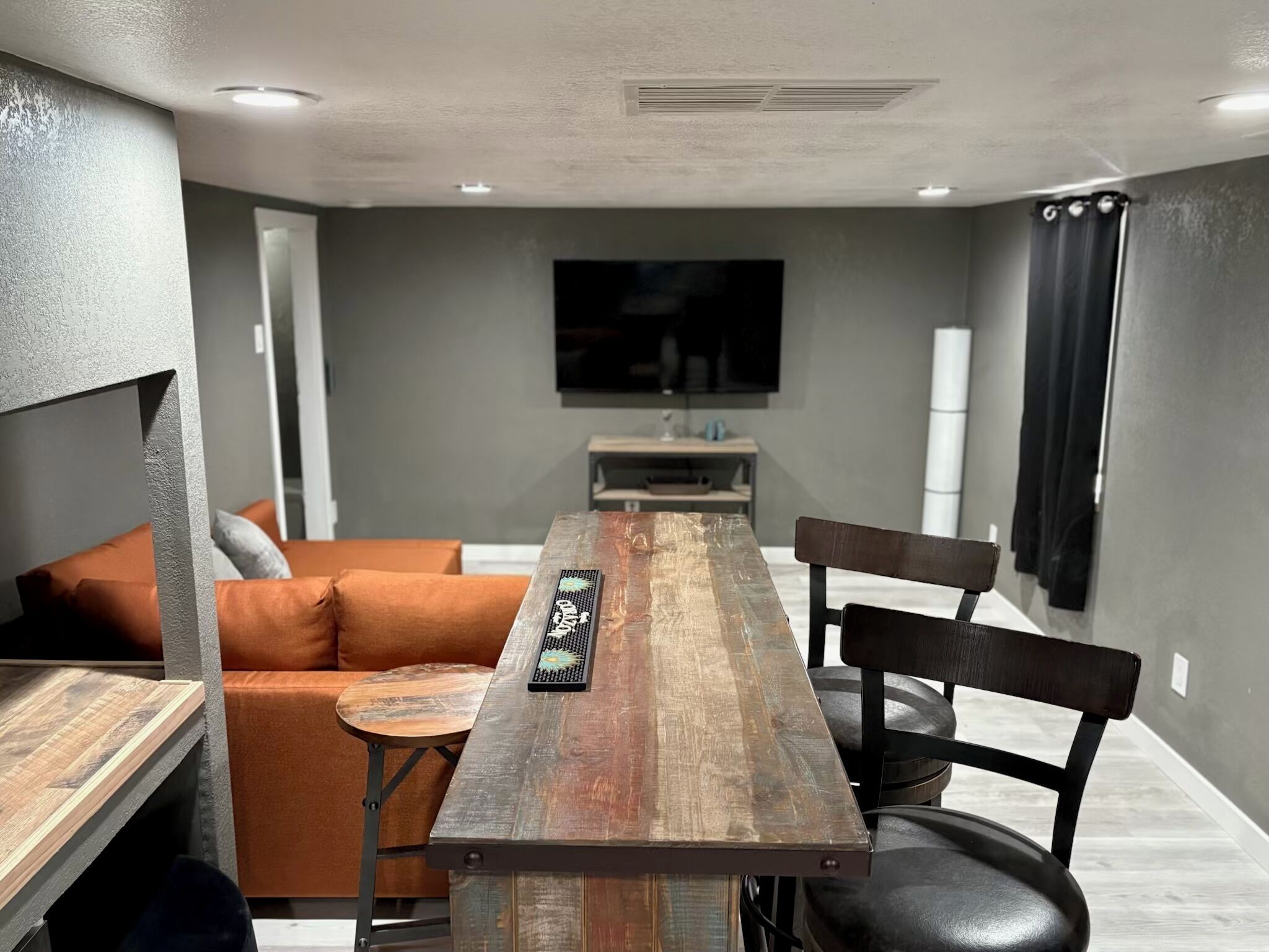 A modern living room with a wooden dining table, a sofa, and a TV mounted on the wall.