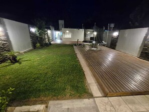 Un espace extérieur bien éclairé, doté d’une terrasse en bois, d’une pelouse et d’un mur en pierre.