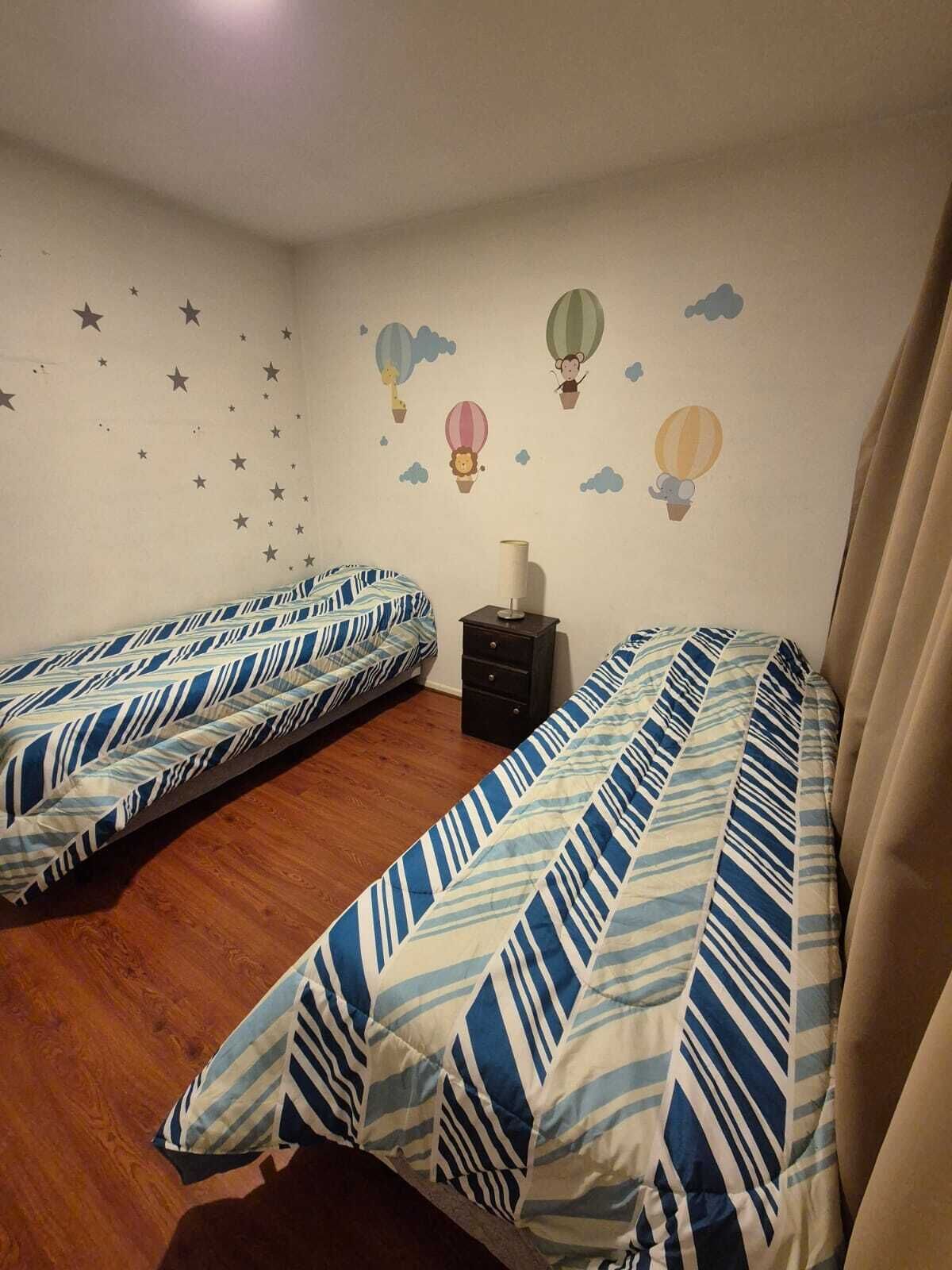 Une chambre avec deux lits simples, une table de chevet et un mur décoré d’étoiles et de montgolfières.