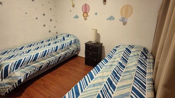 Une chambre avec deux lits simples, une table de chevet et un mur décoré d’étoiles et de montgolfières.