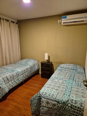 Une chambre avec deux lits, une petite table de chevet, un appareil de climatisation et un rideau.