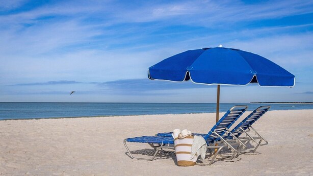 Uma praia com duas cadeiras de praia azuis e um guarda-sol azul.