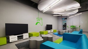 En moderne lounge med to store fladskærme, grønne og blå siddemøbler samt et unikt loftdesign.