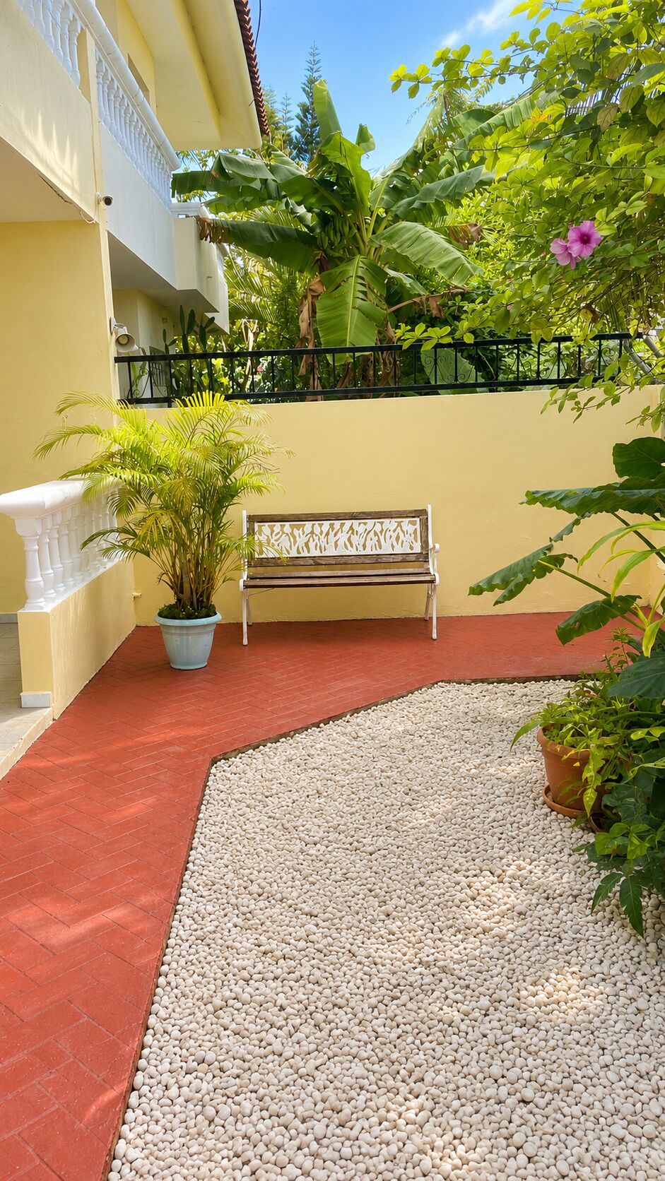 A courtyard with a bench, potted plants, and a pebbled area.