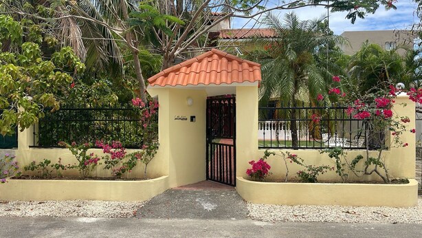 A small building with a tiled roof, surrounded by a black metal fence and flowering plants. - Sweet Home Punta Cana Guest House (Punta Cana)