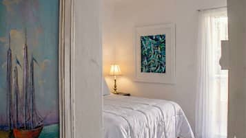 A hotel room with a bed, a painting of sailboats, a lamp, and a window with curtains.