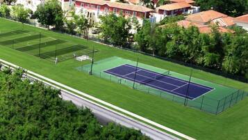 Vista aérea de un barrio residencial con cancha de tenis rodeada de casas y vegetación.