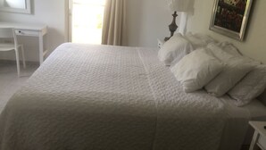 A neatly made bed with white bedding in a room with a desk and a lamp. - Sweet Home Punta Cana Guest House (Punta Cana)