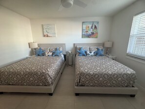 A hotel room with two beds, each with patterned bedding and starfish pillows, a small table with a lamp, and artwork on the walls. - Beautiful Oceanfront 2/2 Condo, Private Balcony, Beachfront pool, No-Drive Beach (Daytona Beach)
