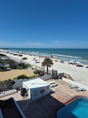 A beach view with a pool area, lounge chairs, and umbrellas. - Beautiful Oceanfront 2/2 Condo, Private Balcony, Beachfront pool, No-Drive Beach (Daytona Beach)