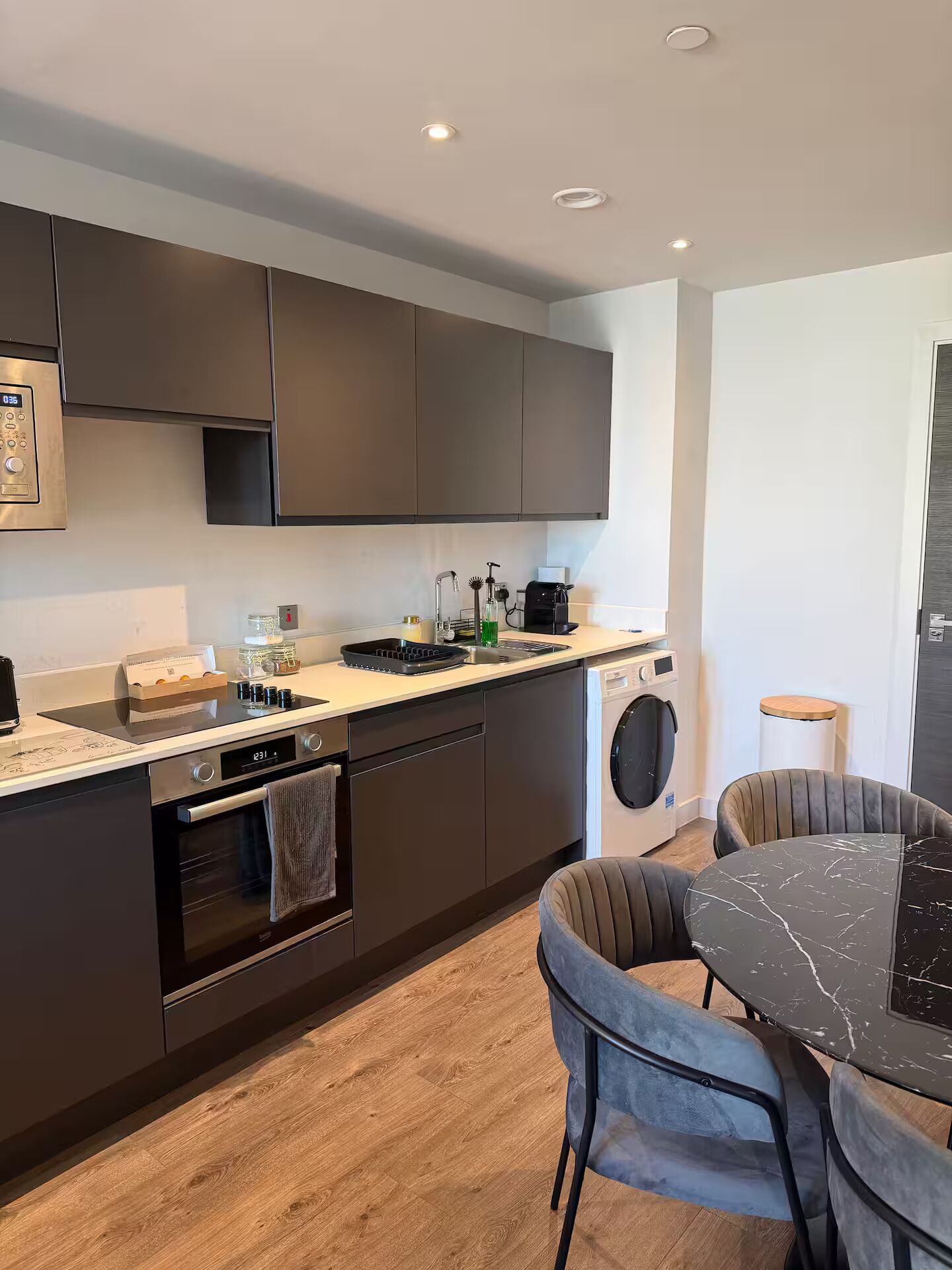 A modern kitchen with dark cabinets, a built-in oven, a dishwasher, and a coffee machine.