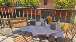 Eine Terrasse im Freien mit einem Holztisch, einem Buch, einer Kaffeekanne und einem Blumentopf.