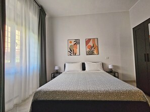 Een hotelkamer met een bed, twee nachtkastjes, een kledingkast en twee abstracte schilderijen aan de muur.