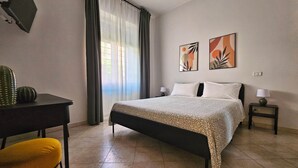 Ein Hotelzimmer mit Bett, zwei Nachttischen, einem Schreibtisch, einem Stuhl und Bildern an der Wand.