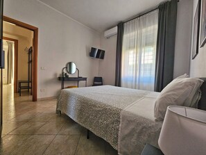 Una habitación de hotel con cama, escritorio con espejo, televisor y una silla.