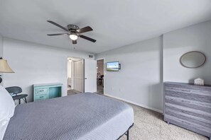 Ein Schlafzimmer mit einem Bett, einem Deckenventilator, einem Fernseher und einer Kommode.