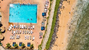 Vista aerea di un resort con piscina, lettini prendisole e spiaggia.