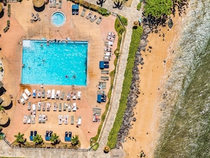 Eine Vogelperspektive zeigt ein Resort mit Schwimmbad, Liegestühlen und einem Strandbereich.