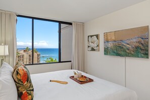Ein Hotelzimmer mit Bett, einem Fenster mit Meerblick, einem Bild an der Wand und einem Tablett mit Frühstücksgebäck.