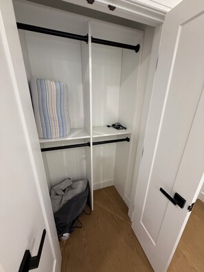Ein weißer Kleiderschrank mit einem gestreiften Kissen auf der obersten Ablage, einem schwarzen Kabel auf der mittleren Ablage und einer grauen Tasche auf der untersten Ablage.