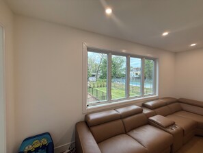 A room with a large window, a brown leather sofa, and a small blue chair with a cartoon design. - Luxury 8BR Estate Heated Pool Walk to Shuls (Long Branch)