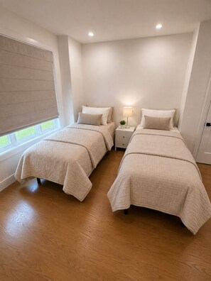 A bedroom with two beds, a bedside table with a lamp, and a window with blinds. - Luxury 8BR Estate Heated Pool Walk to Shuls (Long Branch)