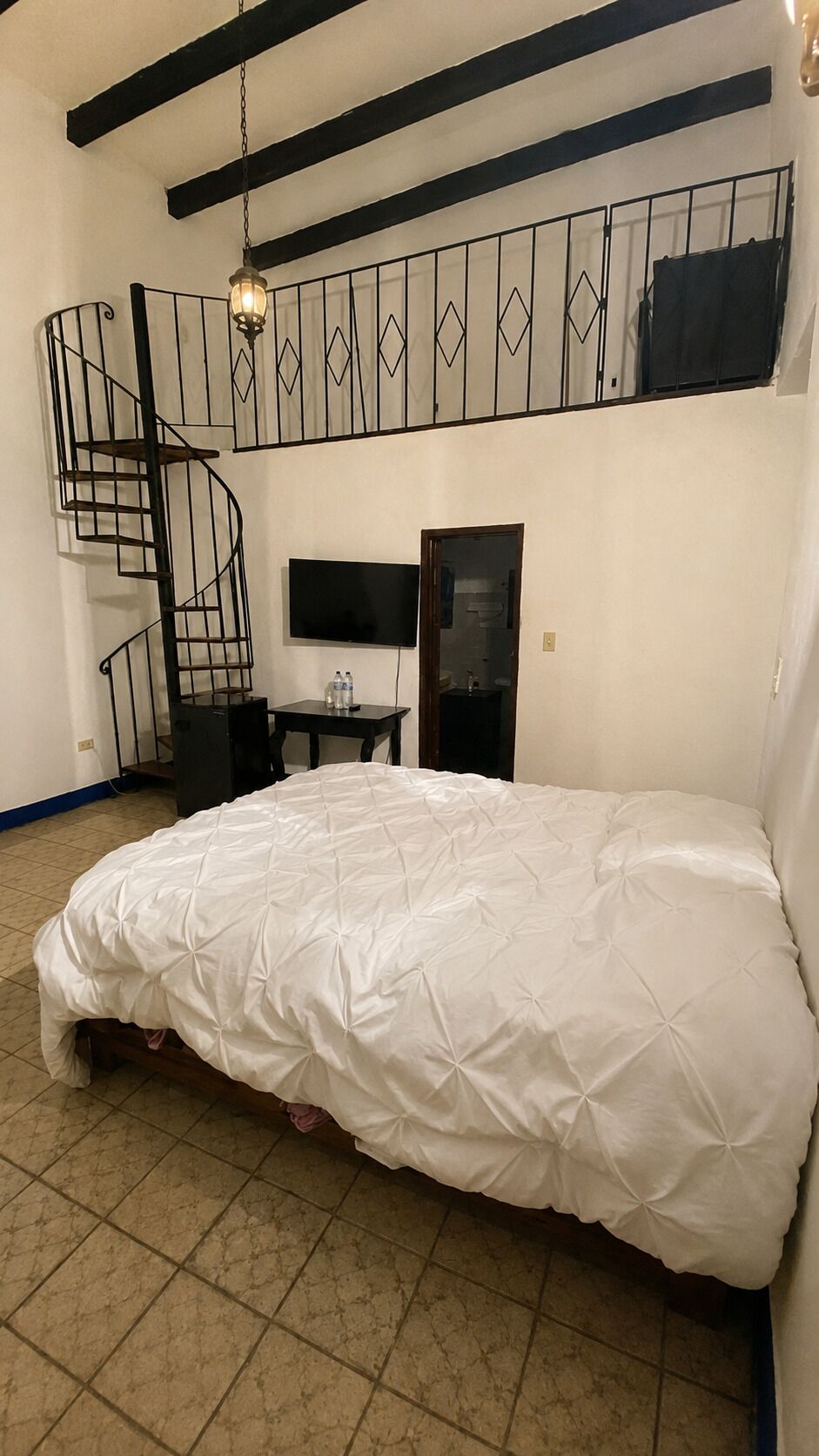 Un dormitorio con literas, un escritorio con silla, un televisor y una escalera de caracol.