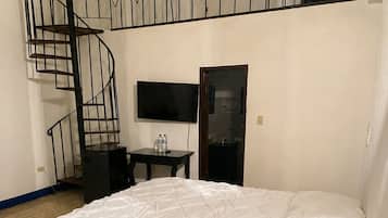 Un dormitorio con literas, un escritorio con silla, un televisor y una escalera de caracol.