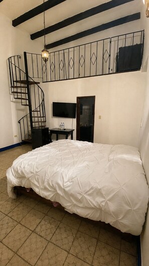 A bedroom with a bunk bed, a desk with a chair, a TV, and a spiral staircase.