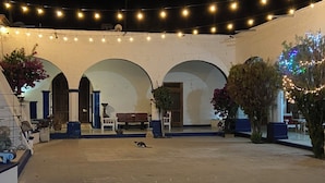 An outdoor courtyard with a white brick wall, arches, string lights, and potted plants. - Casa Roberto Hotel (Álamos)