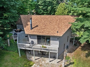 Ein zweistöckiges Haus mit einer Holzterrasse, einem Schornstein und einem umzäunten Garten.