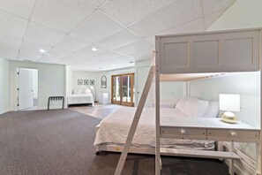 A spacious bedroom with a bunk bed, a bedside table with a lamp, and a large window offering a view of the outdoors. - Luxury Resort Home | Golf, Ski & Lake Bellaire (Bellaire)