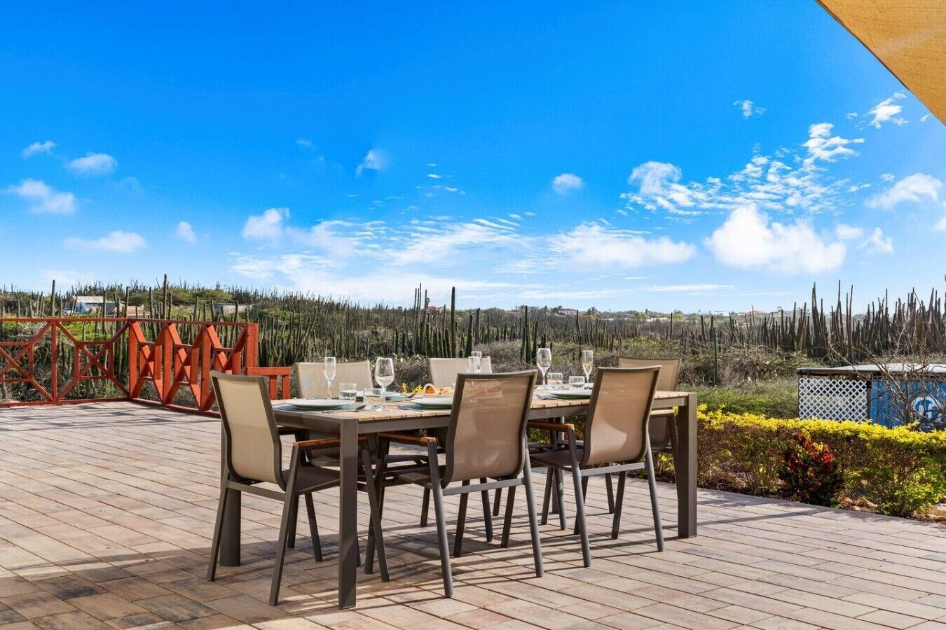 An outdoor dining area with a table set for four, surrounded by chairs, overlooking a landscape with cacti and a fence.