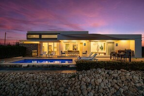 Una casa moderna con piscina, mobiliario exterior y un patio.