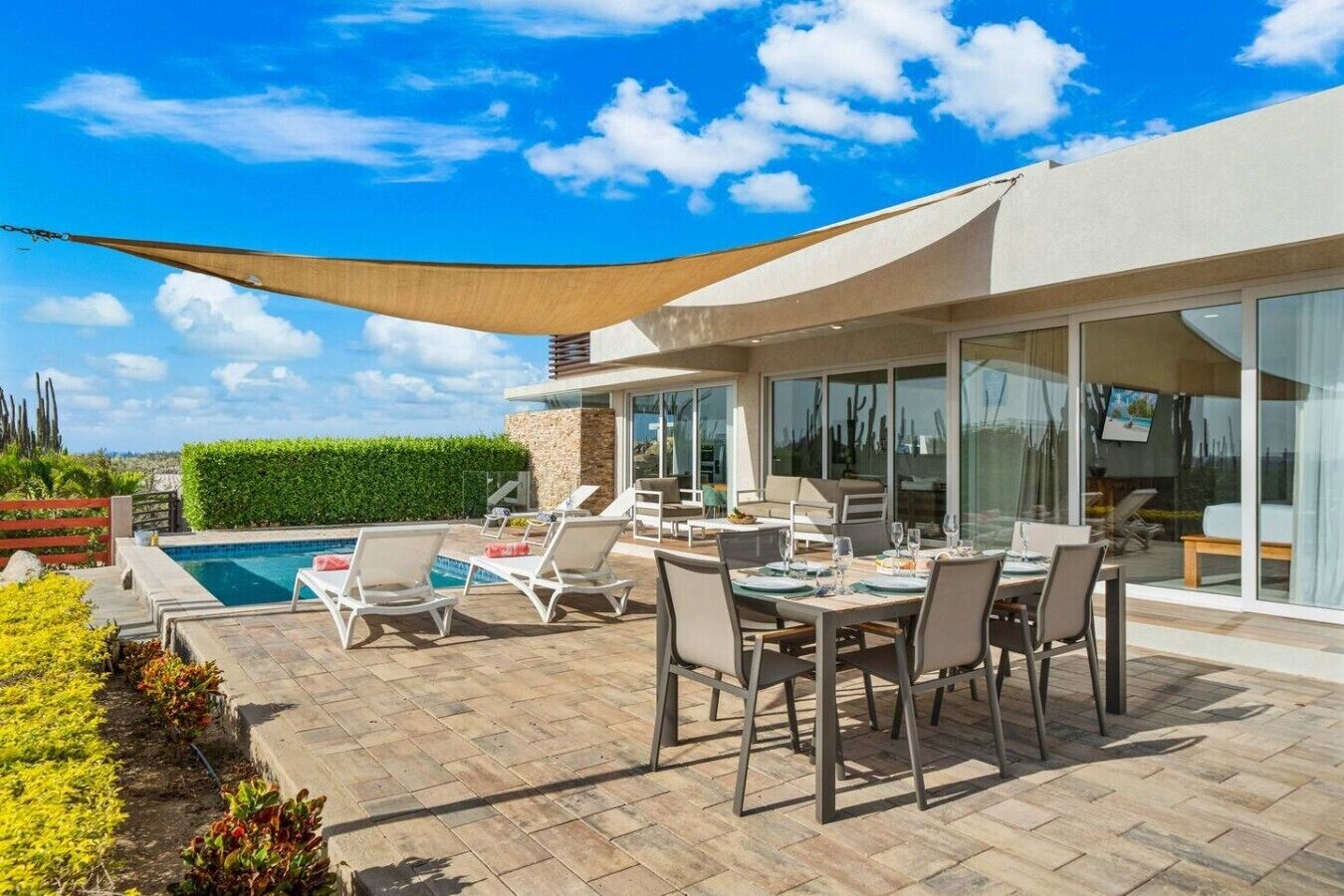 A modern outdoor dining area with a pool, lounge chairs, and a large umbrella.
