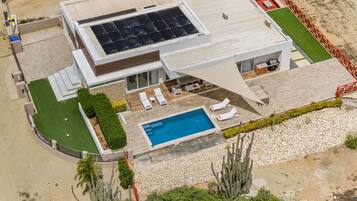 Una casa moderna con piscina, un patio cubierto y un conjunto de paneles solares.