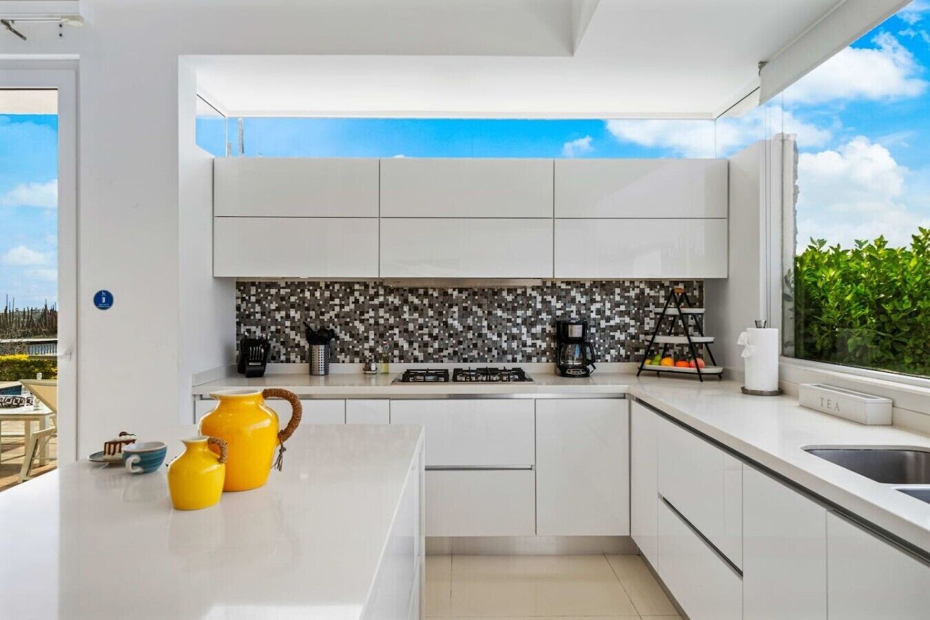 A modern kitchen with white cabinets, a tiled backsplash, and a view of greenery outside.