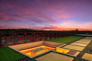 Un espacio al aire libre con una cerca geométrica, una fuente rectangular y un camino con diseño.