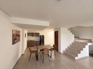 A modern apartment with a dining area, kitchen, and staircase.