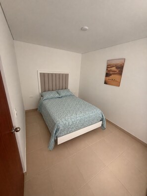 A bedroom with a bed, a door, and a wall-mounted picture.