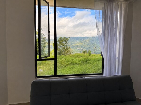 A room with a large window, a sofa, and a view of a green landscape.