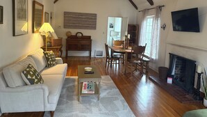 Uma sala de estar espaçosa com teto alto, vigas de madeira, lareira, televisão e área de jantar.