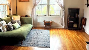 Uma sala de estar acolhedora com um sofá verde, uma mesa de madeira pequena, um abajur e uma estante de livros.
