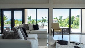 Un salon spacieux avec un canapé blanc, une table basse et une vue sur l’océan grâce à de grandes fenêtres.