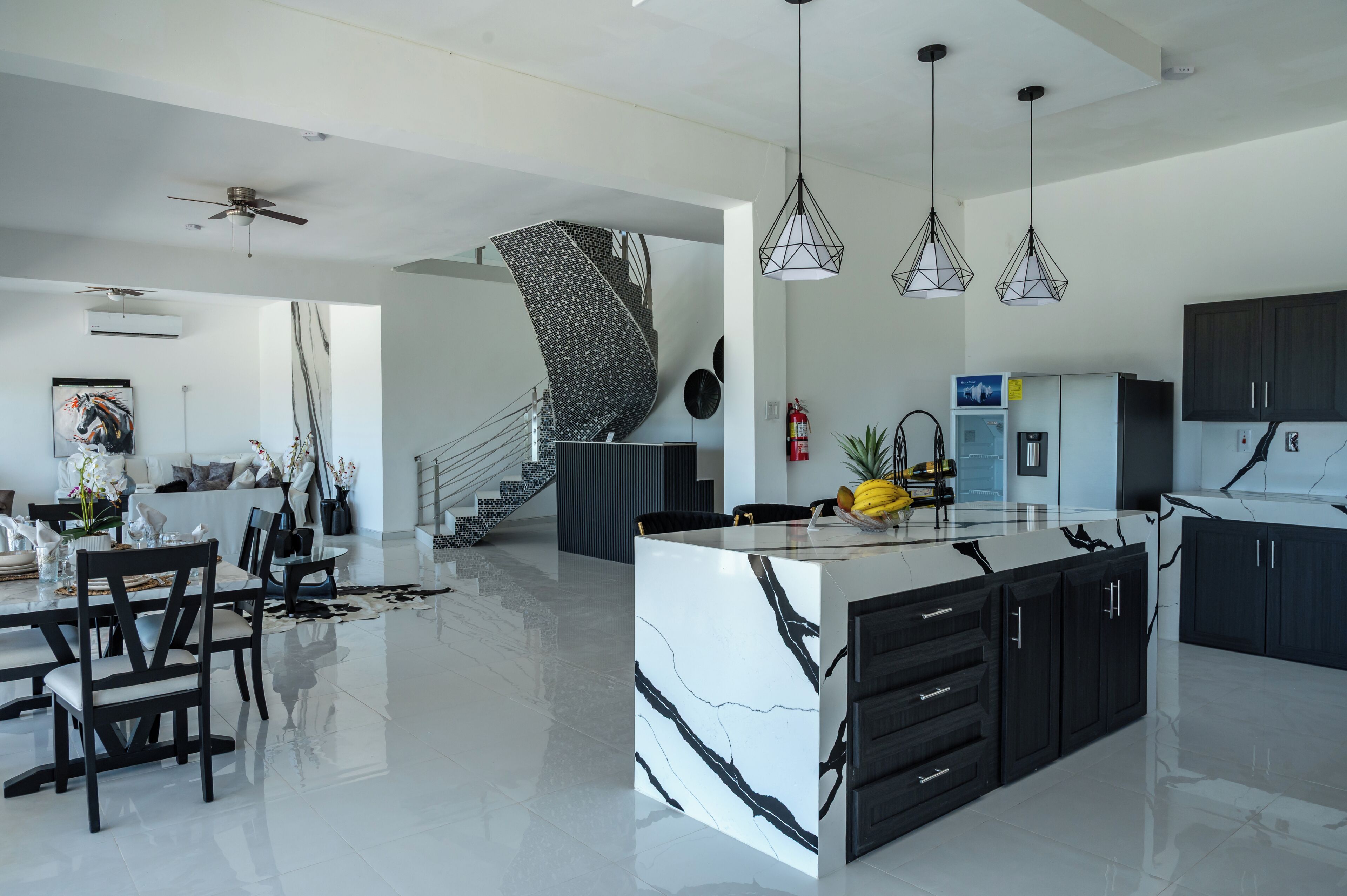 A modern kitchen with a central island, black cabinets, and a white marble countertop.