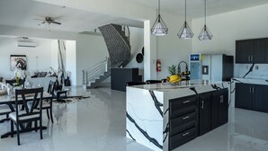 Une cuisine moderne dotée d’un îlot central, de meubles de couleur noire et d’un plan de travail en marbre blanc.