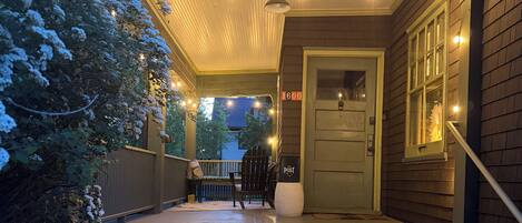 A covered porch with steps leading to a door, string lights, and a chair.